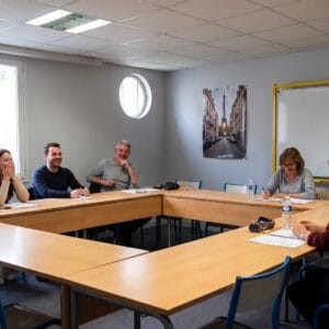 Adulti di età diverse durante un corso di francese all'Alliance Française di Salerno, seduti intorno al tavolo con l'insegnante